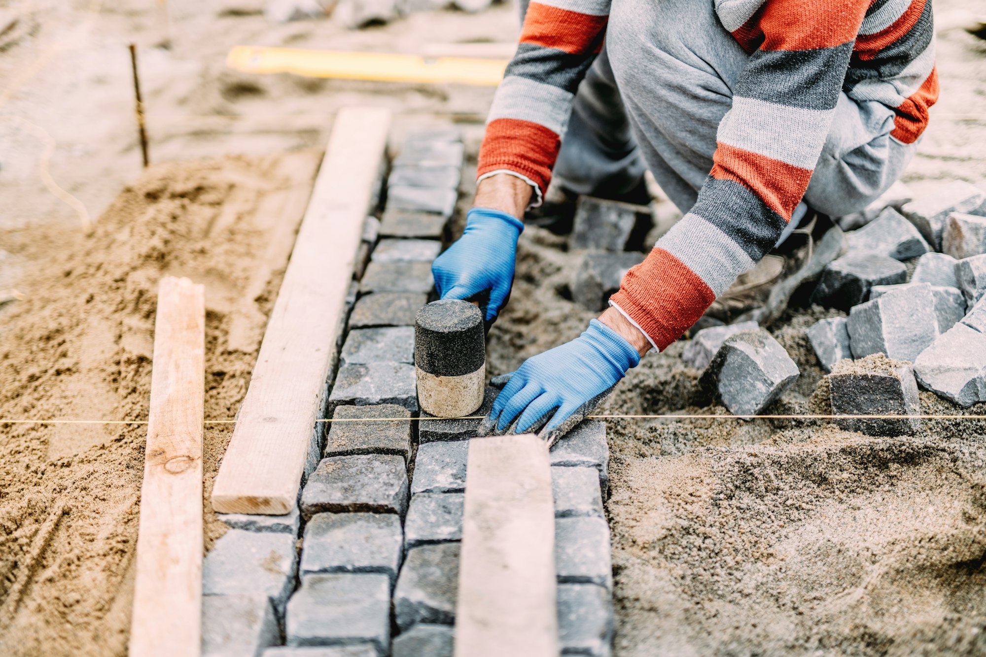 construction worker using industrial tools for stone pavement. granite blocks install details